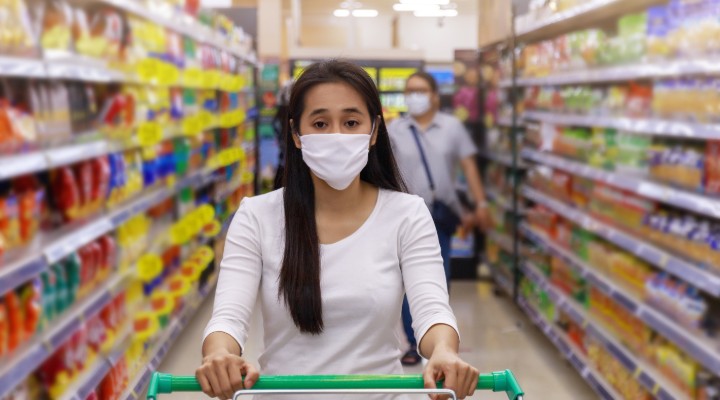 A woman in a grocery store with a face mask pushing a trolley.