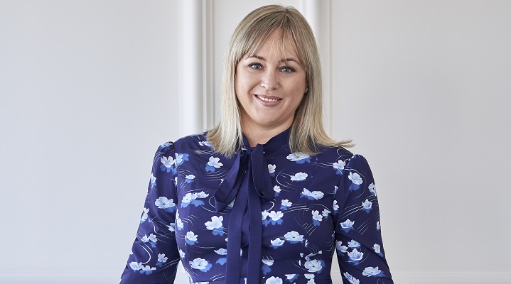 A headshot of a woman with blonde hair and a great blue shirt on.