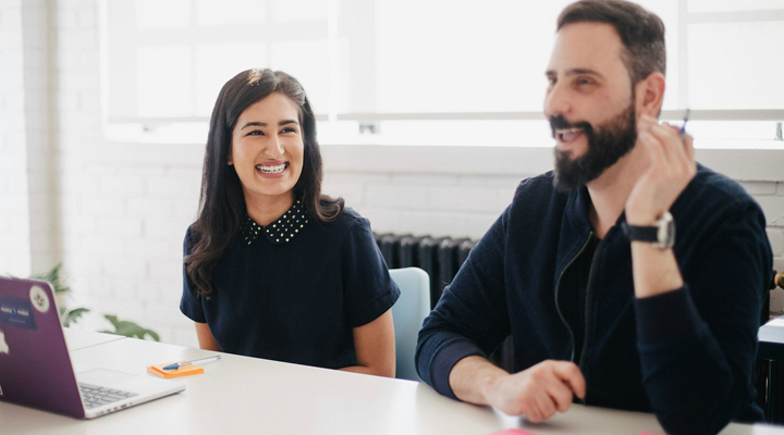 A man and woman sitting next to each other at a large table in an office