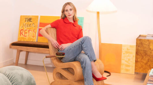 Barrière co-founder Cleo Davis-Urman poses in a chair looking at the camera and wearing a red cardigan and jeans