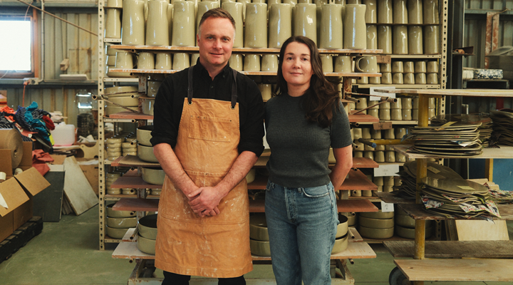 Bobby and Hannah Gordon stand in front of a rack of ceramics in the Robert Gordon factory