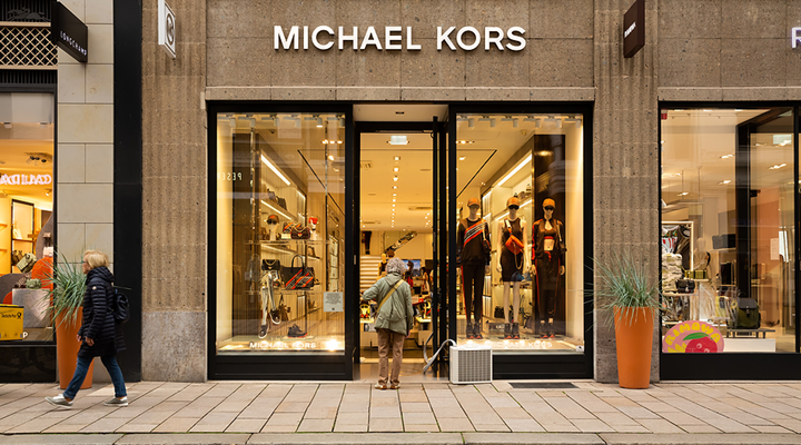 An image of the exterior of a Michael Kors store in Hamburg, Germany, with a woman standing in front of the door.