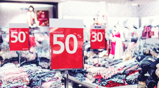 Stacks of folded clothes in a store with red signs offering discounts of 50 and 30 per cent off.