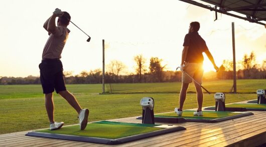 Two men play golf at a Topgolf venue.