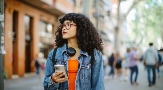 A young woman looking to the side while walking down the street and holding a smartphone