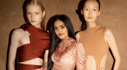 A photo of British-Indian designer Nikita Karizma standing between two models.