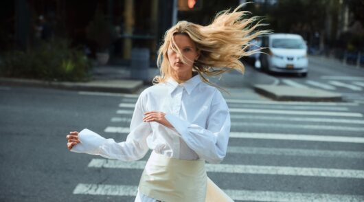 Blonde model running across a crosswalk in white shirt and tie detail belt from Beare Park 2025 campaign photoshoot