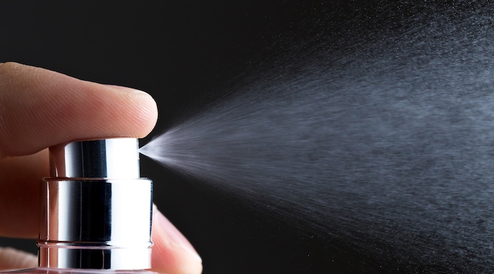 Women's perfume spraying from bottle. Closeup view. Isolated on black background.