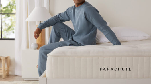 An image from home goods brand Parachute 2024 campaign featuring a man sitting on a Parachute-branded mattress.