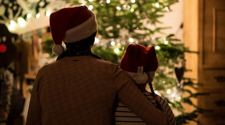 Siblings sitting in front of a Christmas tree wearing Santa hats