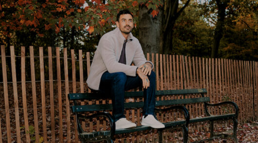 A man sitting on a bench wearing True Classic attire.