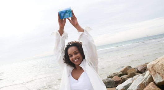 An image of a young woman standing in front of the ocean holding a Conserving Beauty product in her hands.