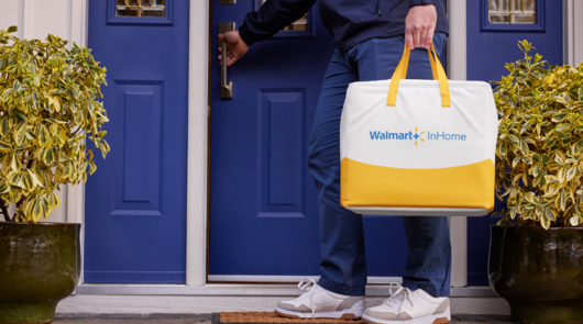 A person carrying a branded tote Walmart tote bag as they walk into the front door of a home