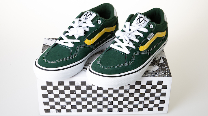 A pair of dark green Vans sneakers atop a checkered-print shoebox.