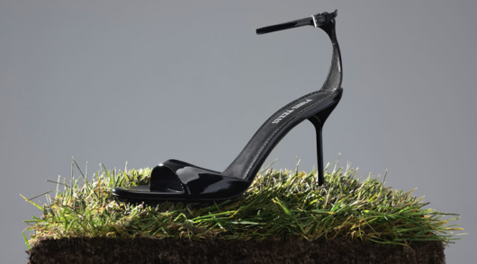 a black high heel displayed on a patch of grass