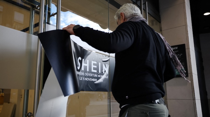 A person sticks a banner with the Shein logo on a glass door