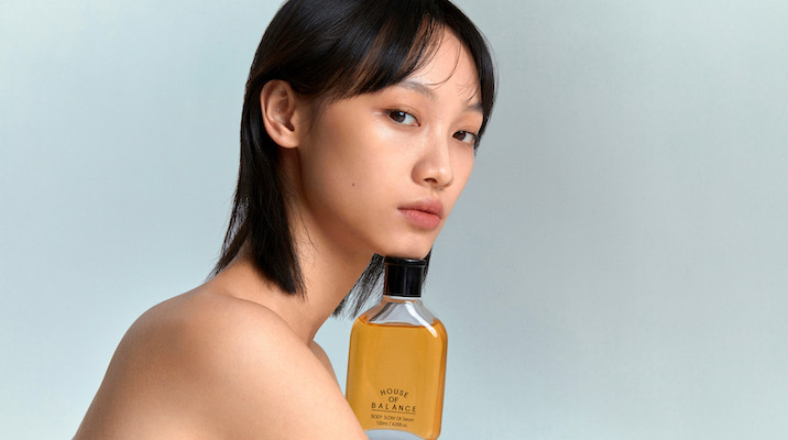 A dark-haired, female model with a House of Balance product underneath her chin.