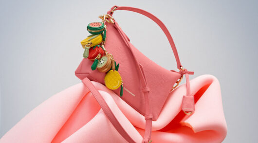 A close-up of a pink Maison de Sabré handbag with several fruit-shaped bag charms.