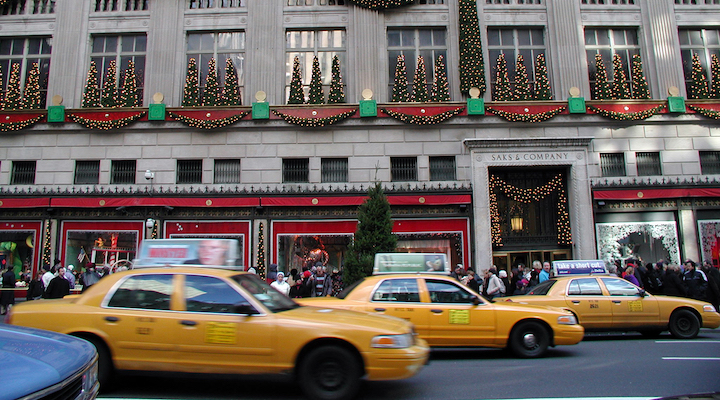 The Saks Fifth Avenue’s Manhattan flagship covered in holiday decorations, with several yellow taxi cabs driving past it.