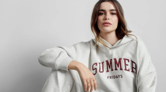 Model Barbie Ferreira sitting in front of a light gray background wearing a gray sweatpant set from Gap x Summer Fridays collection.