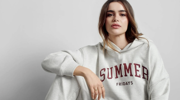 Model Barbie Ferreira sitting in front of a light gray background wearing a gray sweatpant set from Gap x Summer Fridays collection.