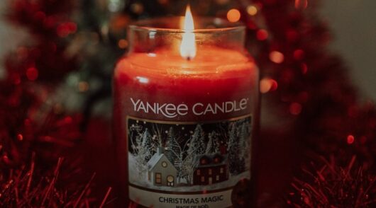 A close-up image of a lit, red Yankee Candle.