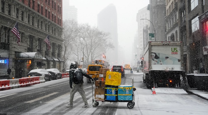 An Amazon delivery worker pulls their cart across the street during snowfall