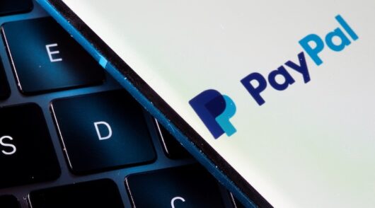 A smartphone with the PayPal logo is placed on a laptop in this illustration