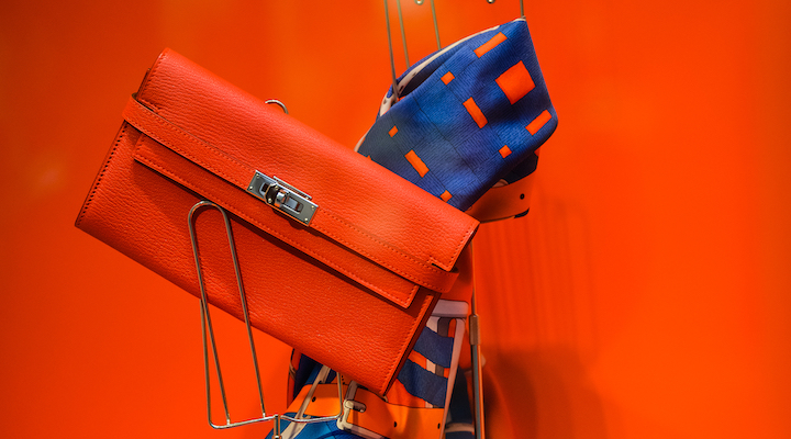 A Hermès window display showcasing a bright orange Hermès bag and silk scarf.