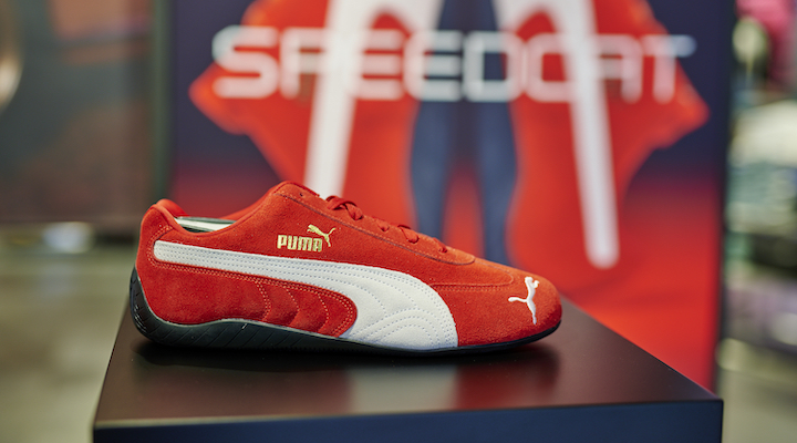 A red Puma Speedcat style placed on a shelf inside a store.