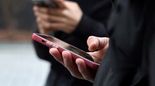 Teenagers look at their mobile phone screens in Paris