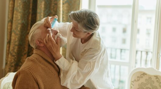 Elderly Woman Putting Eyedrops into the Eyes of an Elderly Man