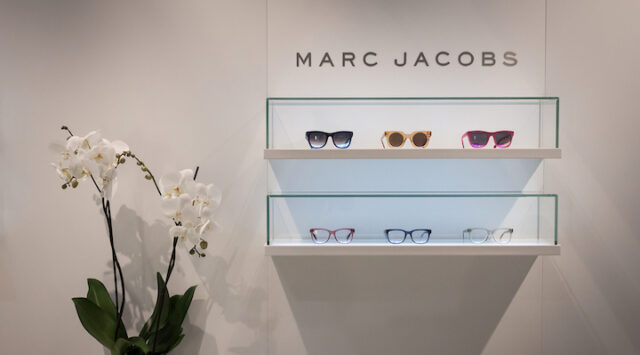 Marc Jacobs sunglasses displayed on a gray wall.