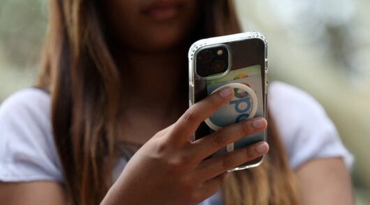 s holding a mobile phone as law banning social media for users under 16 in Australia takes effect
