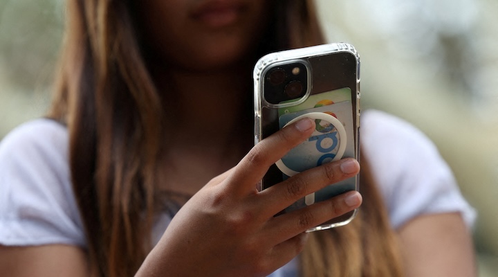 s holding a mobile phone as law banning social media for users under 16 in Australia takes effect