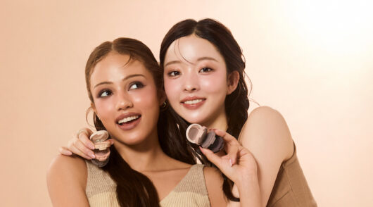 Two female models posing against a light pink background.