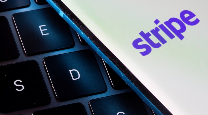 A smartphone with the Stripe logo is placed on a laptop in this illustration