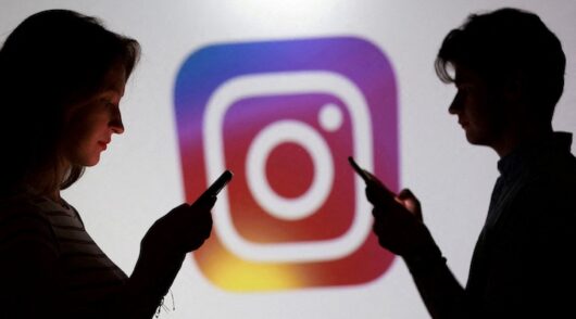 Teenagers pose for a photo while holding smartphones in front of an Instagram logo