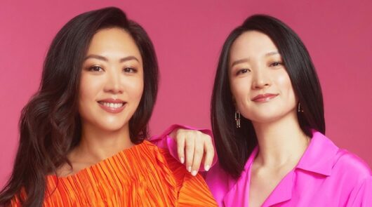 Glow Recipe co-founders Sarah Lee and Christina Chang standing in front of a pink background.
