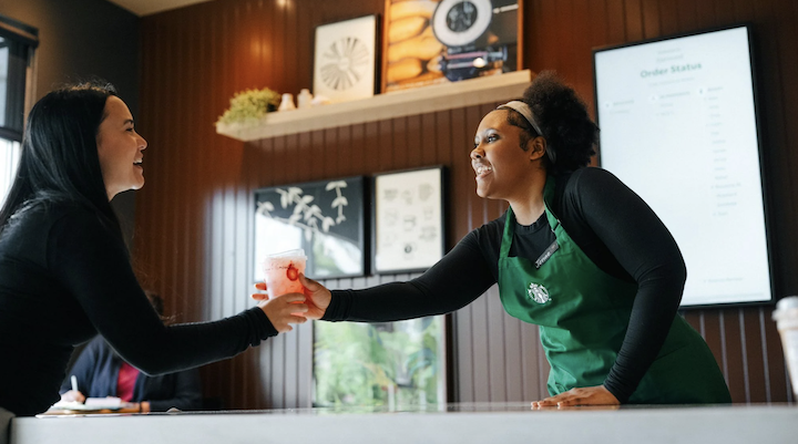 A Starbucks employee handing a customer a drink.