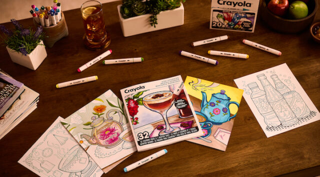 Coloring books and markers from Crayola’s All Grown Up collection laid out on a table.