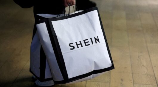 A customer holds shopping bags with a Shein logo in the first physical space of online fast-fashion retailer Shein