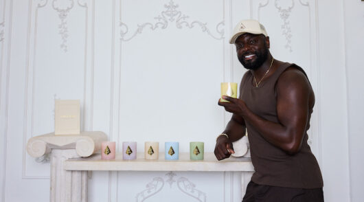 Forever Mood CEO Denis Asamoah holding a candle and standing in front of a white wall.