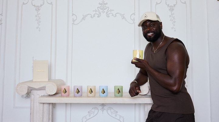 Forever Mood CEO Denis Asamoah holding a candle and standing in front of a white wall.