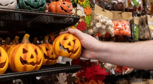 A person’s arm reaching out to pick up a mini-jack-o'-lantern pumpkin off a shelf.
