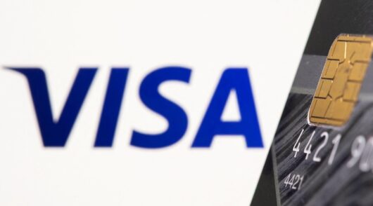 Credit card is seen in front of displayed Visa logo in this illustration.